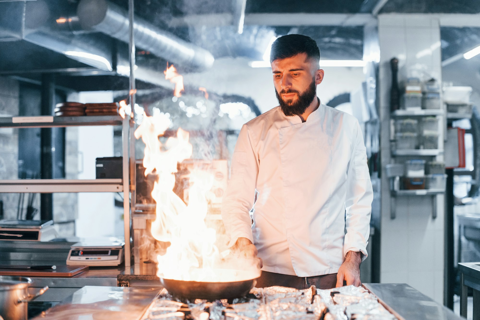 Frying pan is on fire. Chef in white uniform cooking food at kitchen. Busy day at work